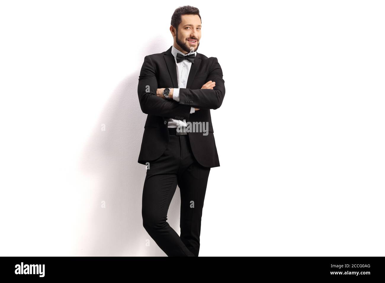 Handsome man in a black suit with bow tie posing on a white background ...