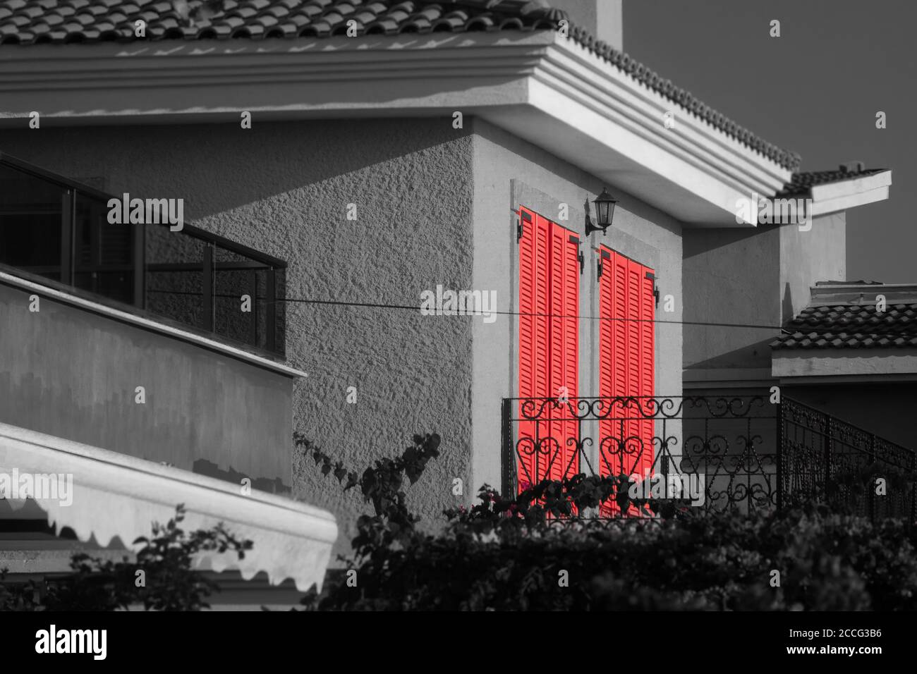 Black and white facade of a village house terrace with red window blinds. Stock Photo