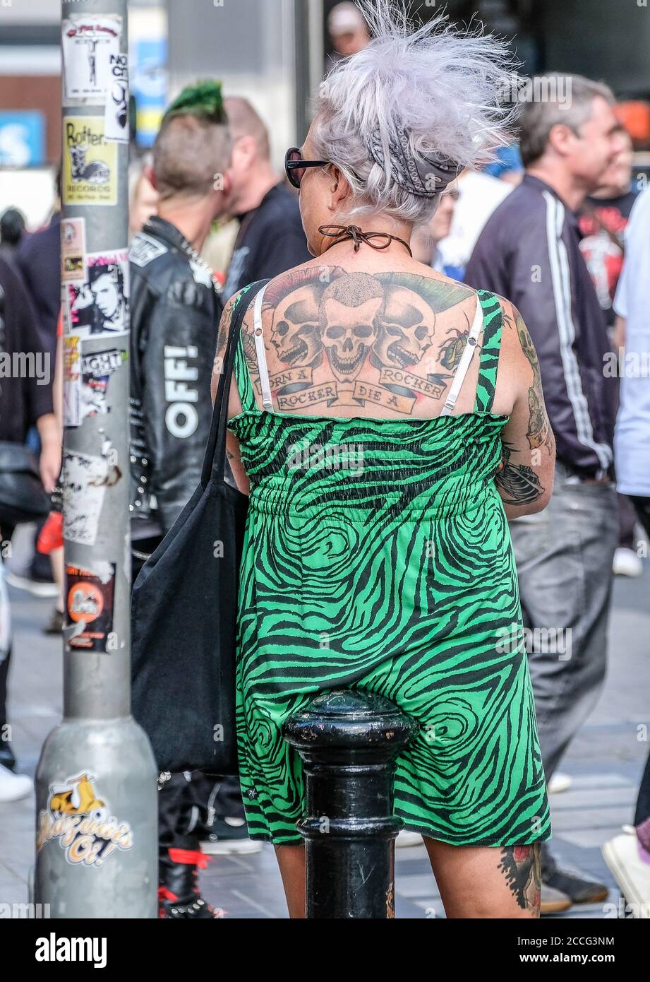 punk woman sitting on low post with bright green dress and vivid tattoos on her back Stock Photo