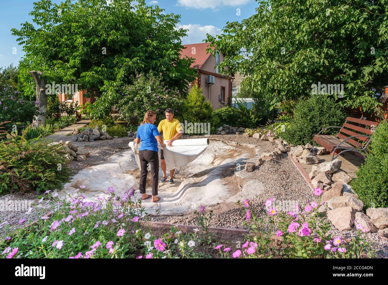 Family roll out a roll of white non-woven geotextile fabric to set up fish pond Stock Photo