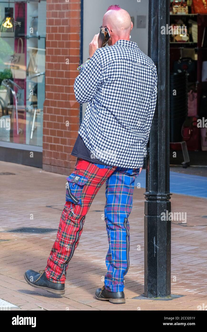 punk leaning against lamp-post and sporting alternate blue/red checked trousers Stock Photo