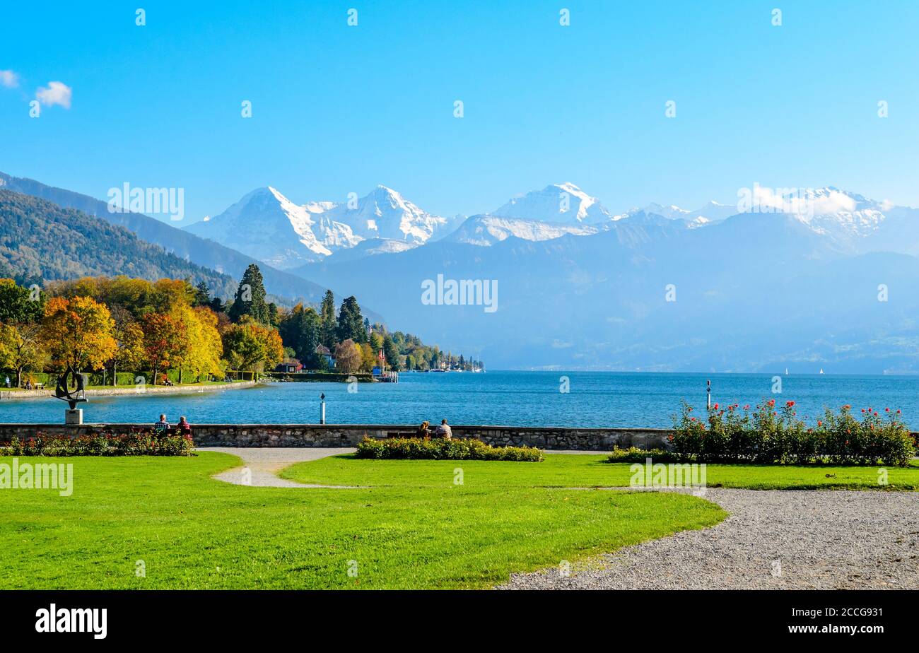 Amazing colorful autumn postcard view on Lake of Thun, Thunersee, alps mountains, mountain Eiger, Jungfrau, Monch (Moench, Mönch), blue sky, trees. Ca Stock Photo