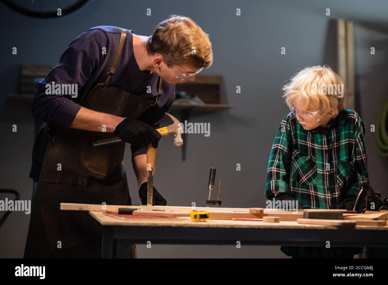 a young male carpenter is teaching woodwork to a young boy in his ...