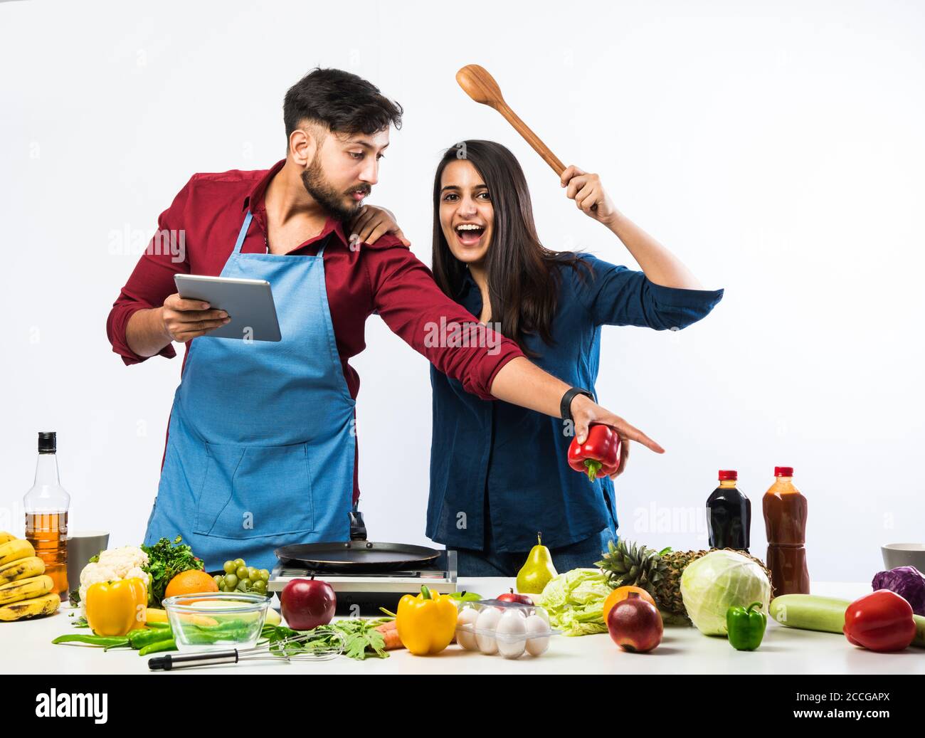 Indian couple in kitchen - Young Beautiful asian wife enjoying cooking with husband with lots of fresh vegetables and fruits Stock Photo