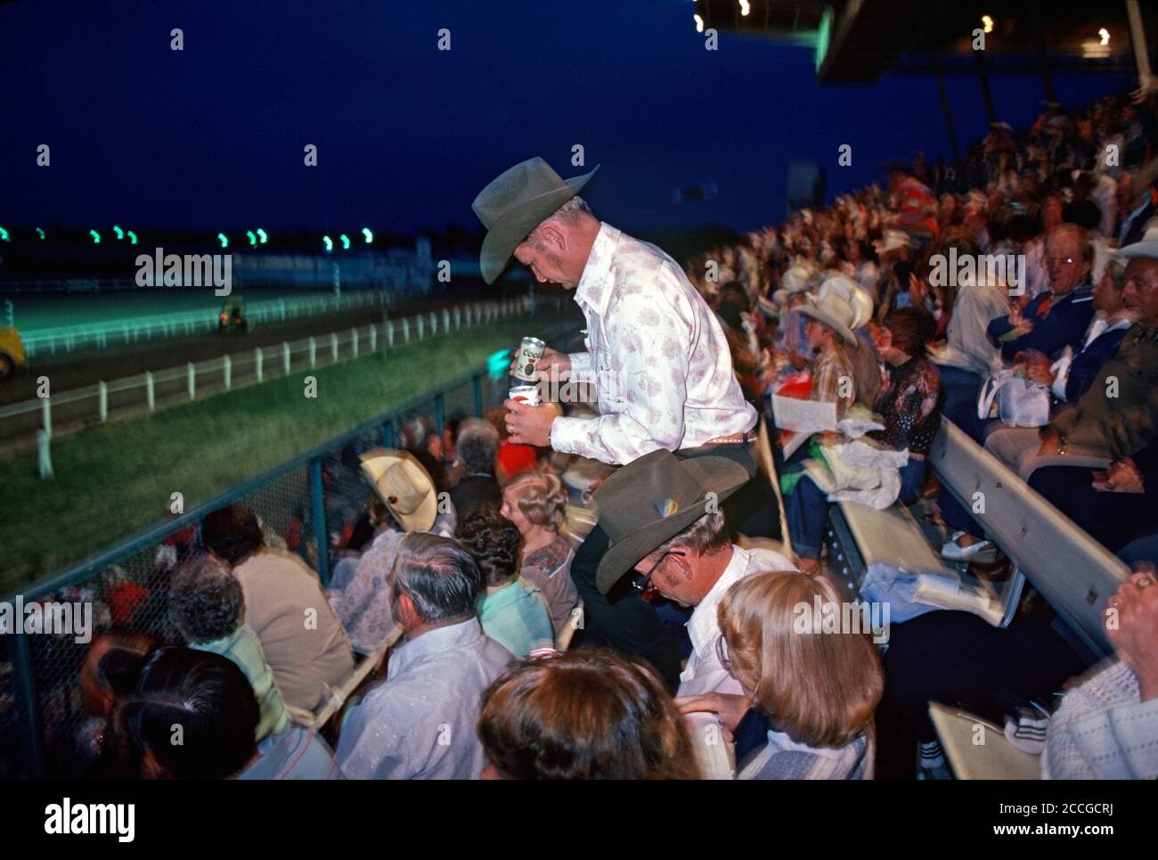 SPECTATOR WITH CANS OF BEER AT BUCKBOARD RACING, CHEYENNE, WYOMING, USA 1970s Stock Photo