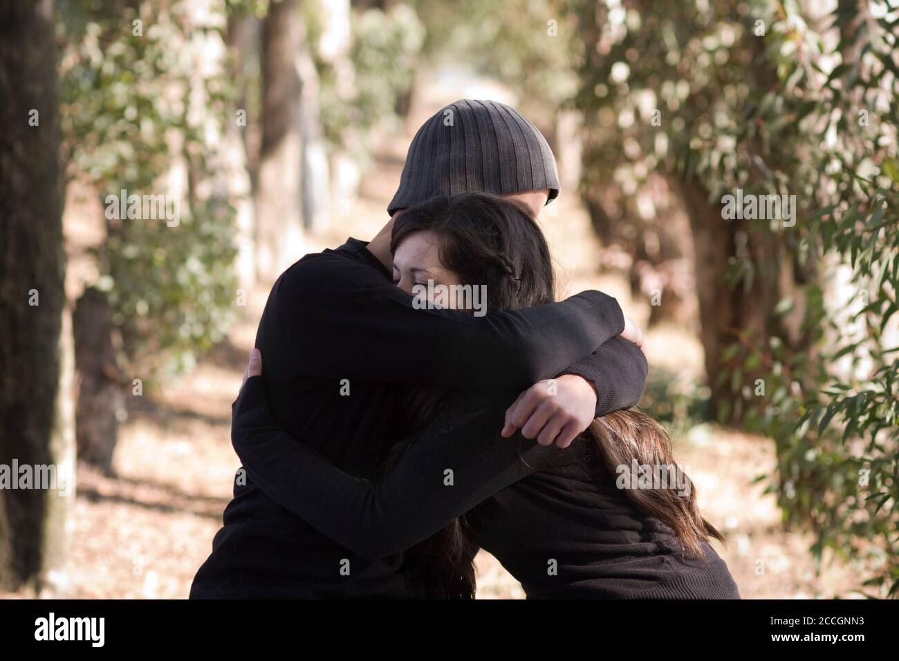 A man and and woman sitting on a park bench embrace. Stock Photo