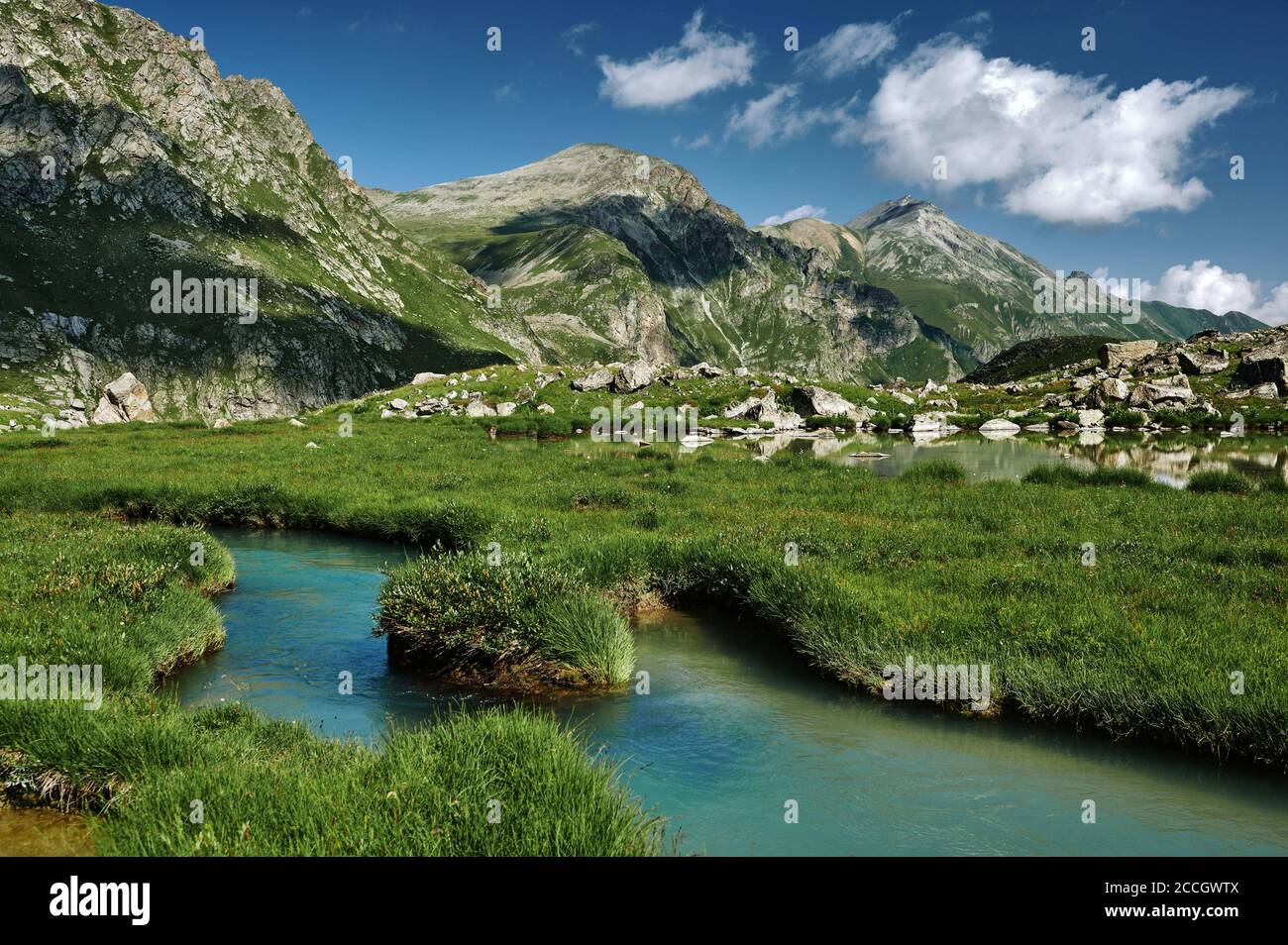 Majestic mountains landscape with blue deep river in green grassy valley. Beautiful wild nature Stock Photo