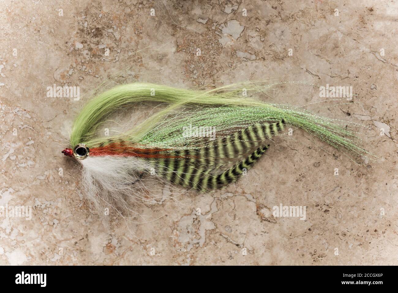 A homemade fishing fly designed for catching pike, Esox lucius. Desaturated colours on a light stone background. Dorset England UK GB Stock Photo