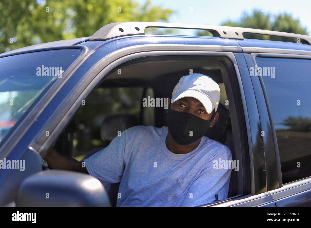 African-American man leaving in his truck wearing a mask to protect him from a virus infection Stock Photo