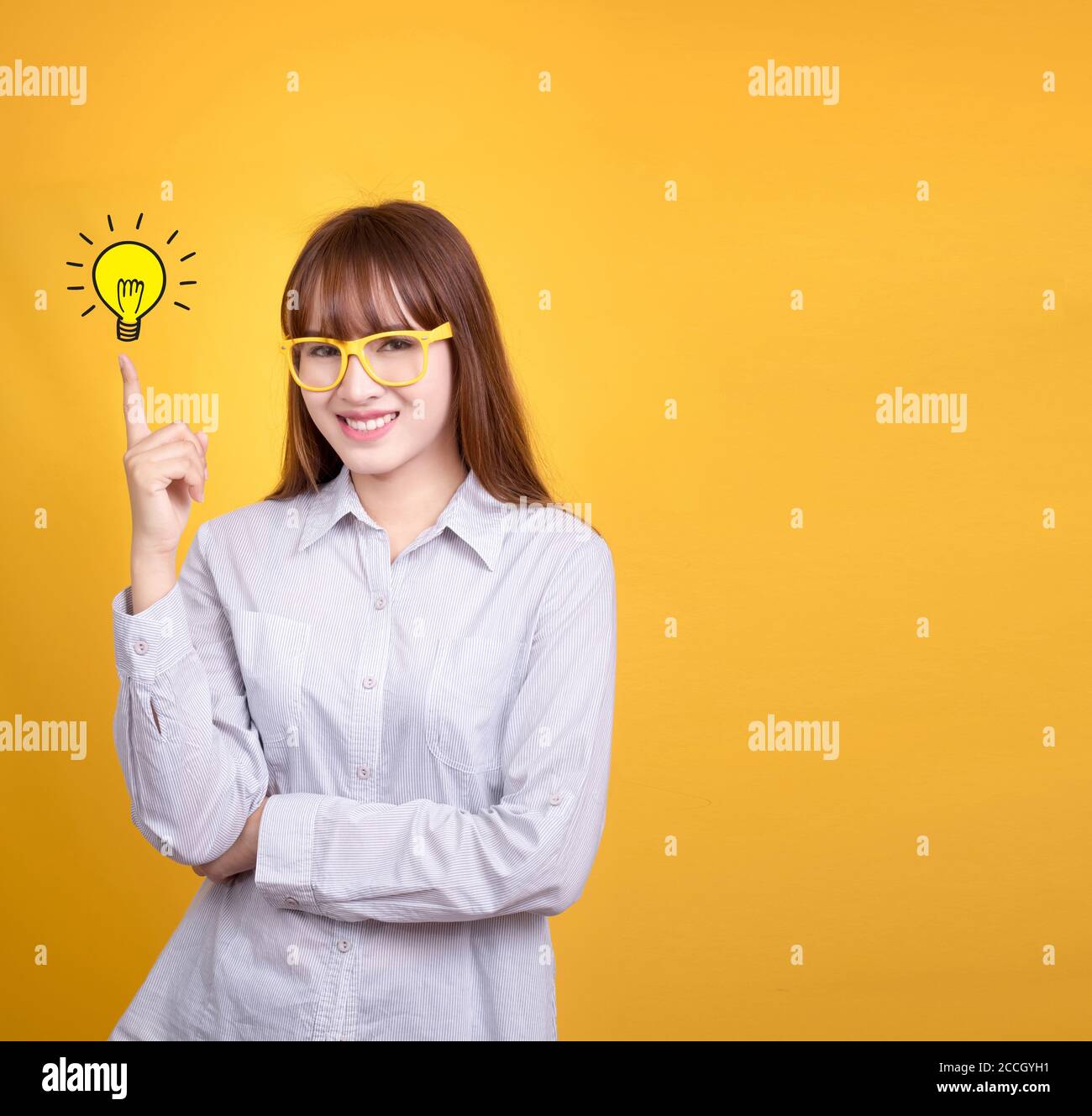Business Asian woman with yellow vintage glasses stand and have idea lamp bulb light on fingertip, yellow background with copy space for design for po Stock Photo