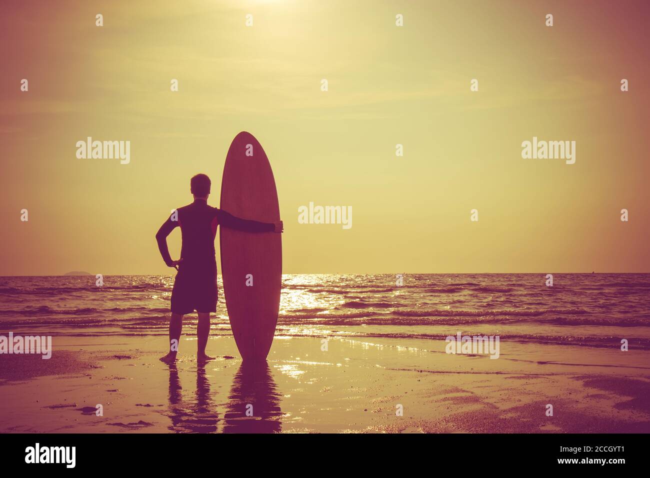 Silhouette of surf man stand with a surfboard. Surfing at sunset beach. Outdoor water sport adventure lifestyle.Summer activity. Handsome Asia male mo Stock Photo
