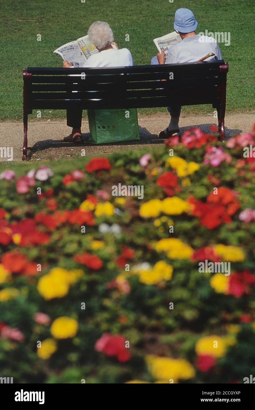 Elderly couple reading newspapers sitting on a park bench. Tower Gardens, Skegness, Lincolnshire, England, UK Stock Photo
