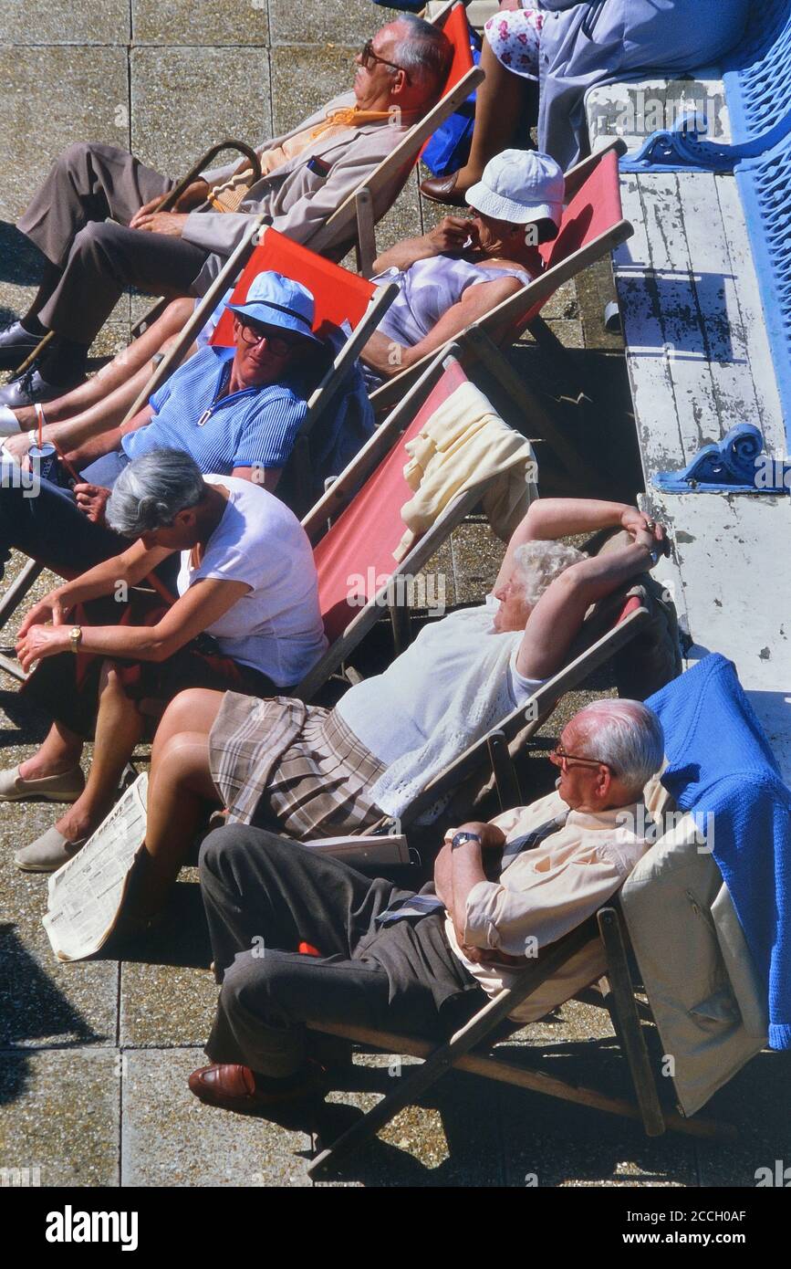 A group of elderly tourists sitting in deckchairs enjoying the summer sunshine. Hastings, East Sussex, England, UK Stock Photo