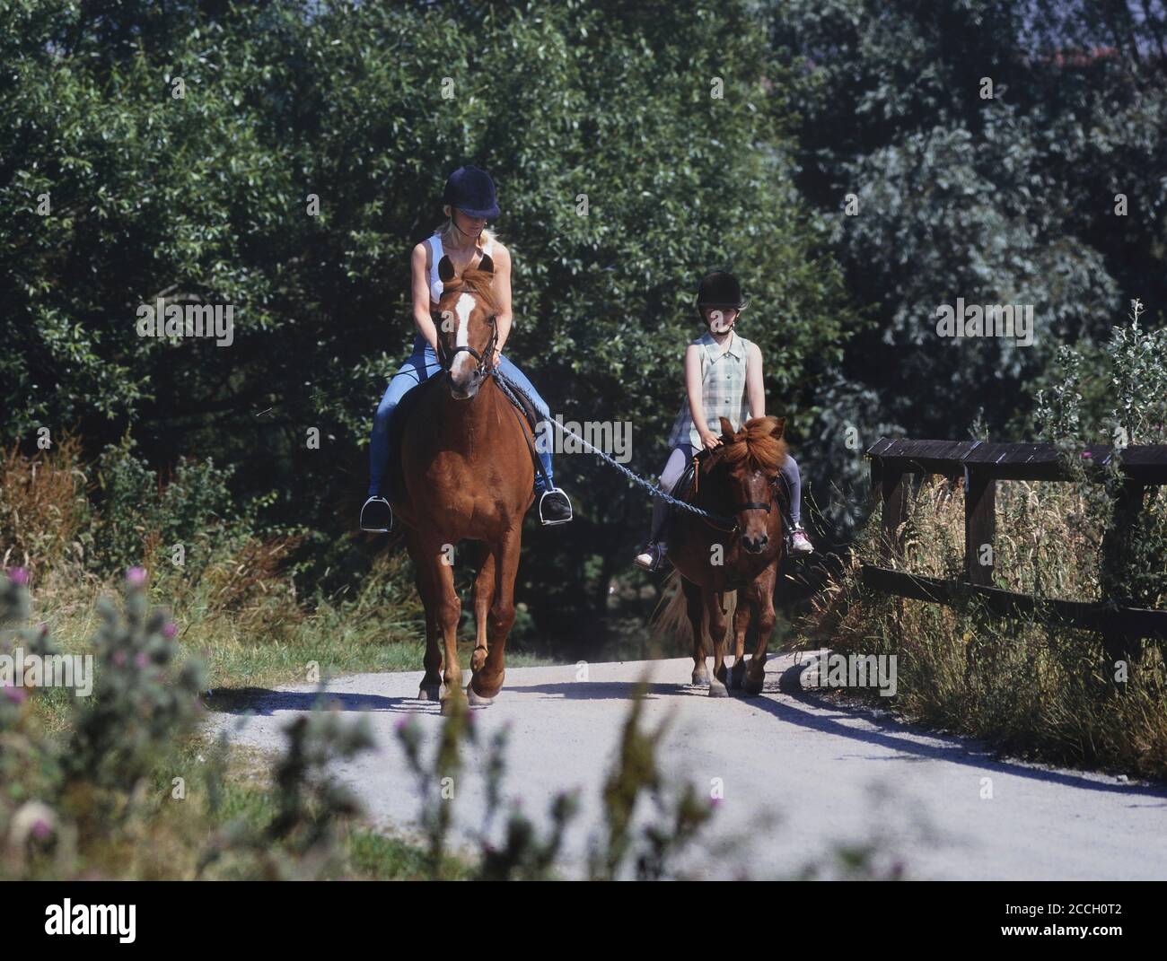 Mother and daughter riding together using a lead rein to train a pony and young horse rider. UK