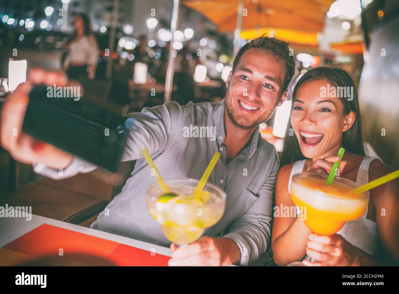 Fun date night out young people taking selfie of themselves drinking giant margaritas cocktails party couple going out on Miami Ocean drive restaurant Stock Photo