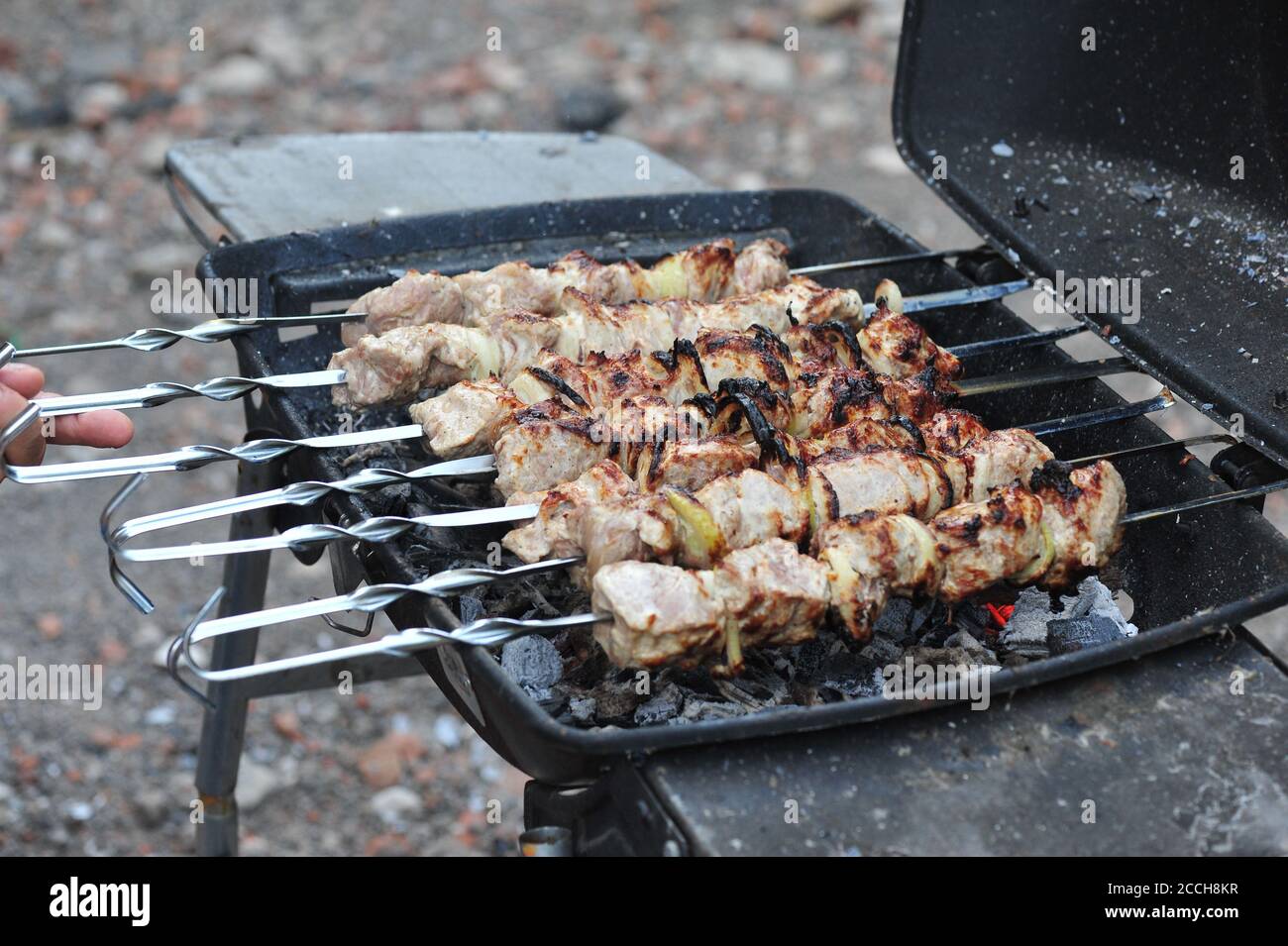 Man's hand turn over kebabs on a grill for better quality of preparation Stock Photo