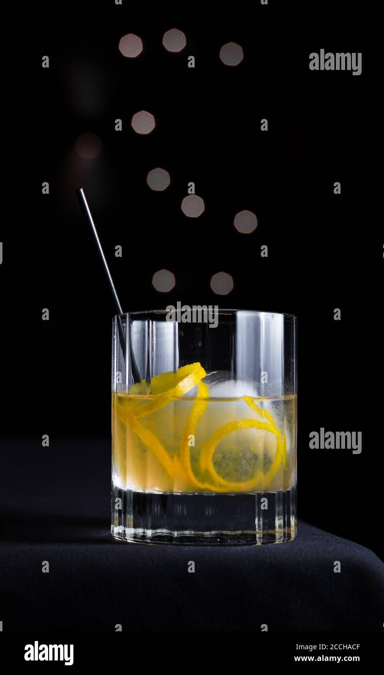https://c8.alamy.com/comp/2CCHACF/hip-sleek-modern-scene-of-craft-cocktail-with-lemon-garnish-ice-sphere-in-rocks-glass-isolated-on-black-background-with-grey-bokeh-circles-2CCHACF.jpg