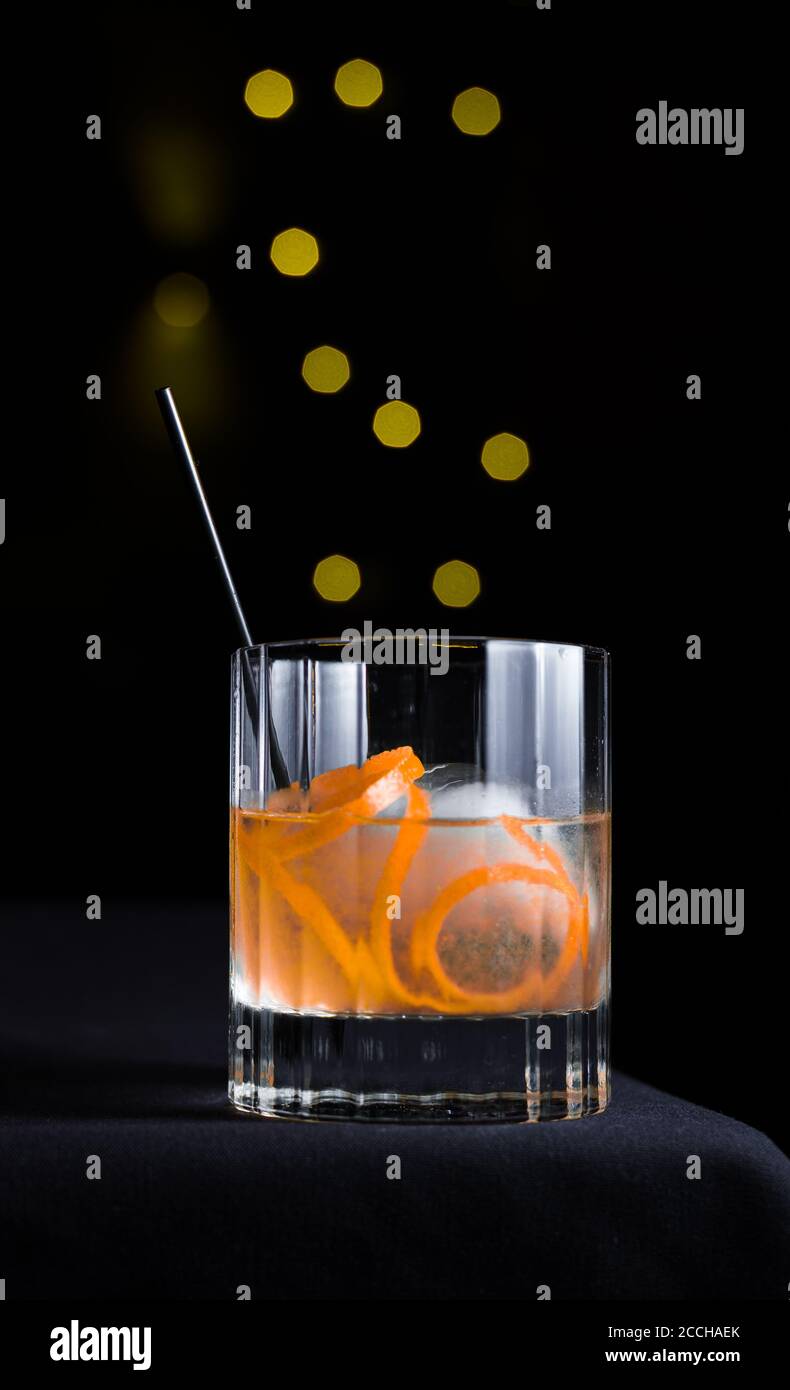 A craft cocktail with orange rind garnish served on the rocks isolated on black background with yellow bokeh circles Stock Photo