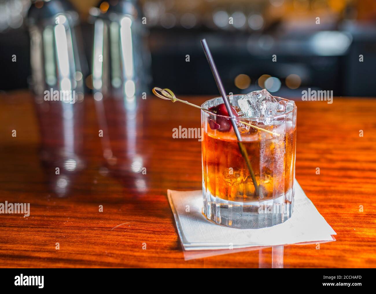 A modern rustic scene of a classic bourbon whisky craft cocktail served on the rocks in a rocks glass with cherry garnish on a wooden bar Stock Photo