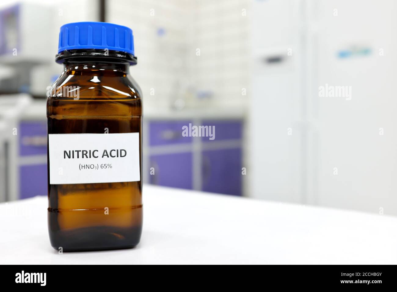Selective focus of strong Nitric acid solution in brown amber bottle. Blur white laboratory backdrop with copy space. Stock Photo