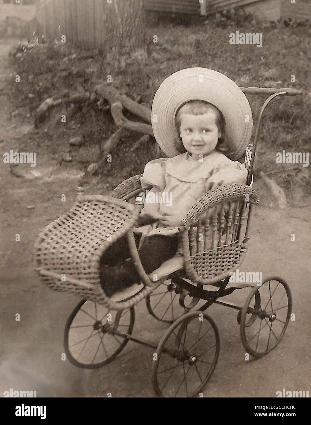 A little girls poses in an antique wicker stroller/tram. circa:  1904-1915 Stock Photo