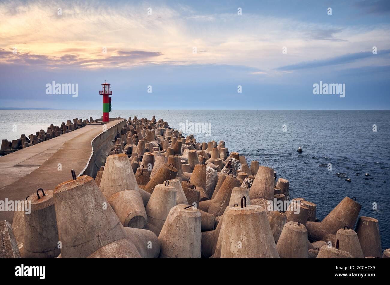 Pier with lighthouse protected by concrete breakwater tetrapods at sunset. Stock Photo