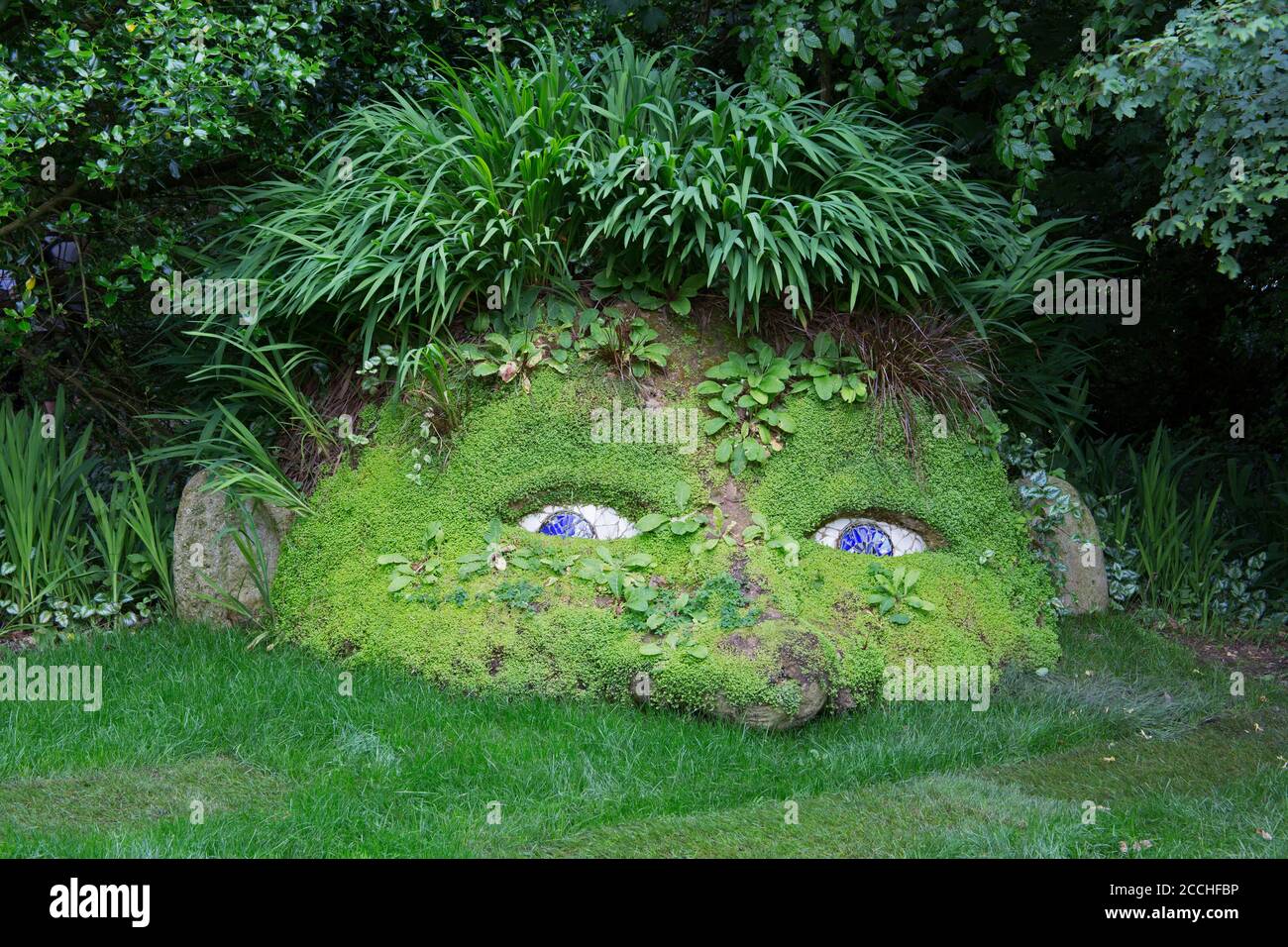 Giant's Head sculpture from mud and plants in woodland garden, Lost