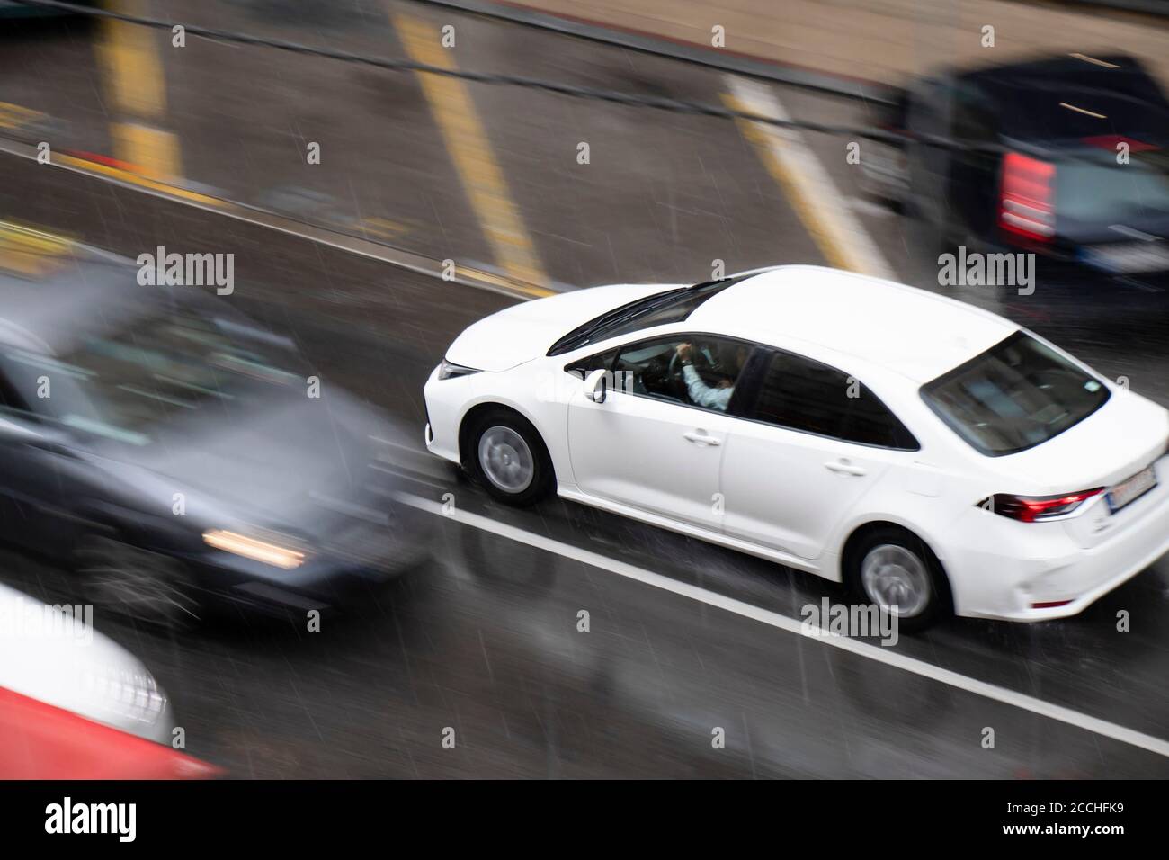 Blurry driving cars on the street hit by the heavy rain with hail, on a rainy day in motion blur panning shot from above Stock Photo
