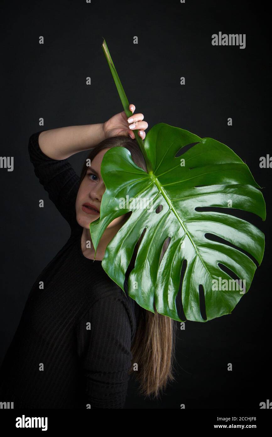 Portrait of beautiful woman with green tropical leaf on black background Stock Photo