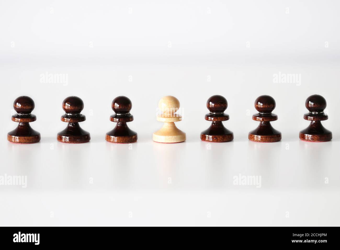Row of black pawn chess pieces with white one in the middle on white background - stand out of the crowd concept Stock Photo