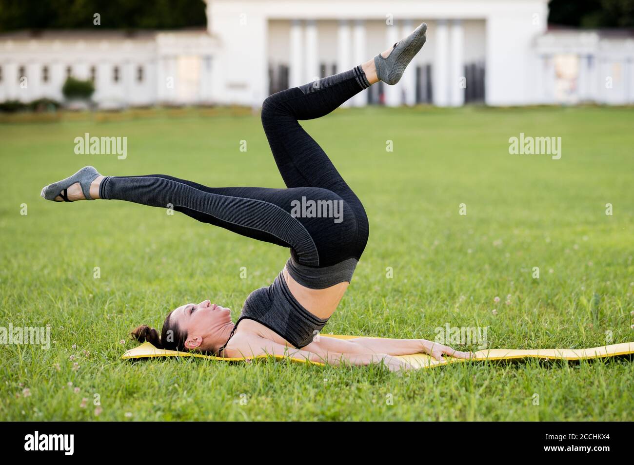 Beautiful young woman lying on a yellow mattress pose while wearing a  tight sports outfit in the park doing pilates or yoga bicycle exercises  Stock Photo  Alamy