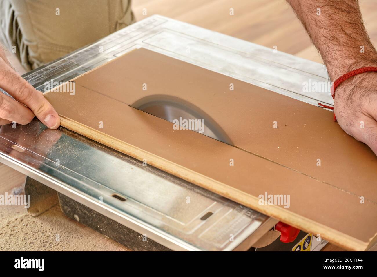 Man cutting laminate floor boards on circular saw, detail on hands holding wooden panel and rotating ring, home improvement illustration photo Stock Photo