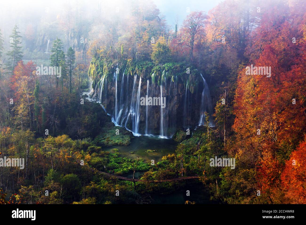 Incredible autumn view on foggy waterfall in Plitvice lakes. Orange forest on background. Plitvice National Park, Croatia. Landscape photography Stock Photo