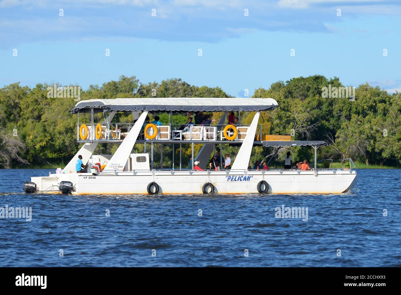 Pelican boat during a sunset cruise on the Zambezi River near Victoria Falls, Zimbabwe with forest in Zambia behind. Boats tour for visitors. Stock Photo