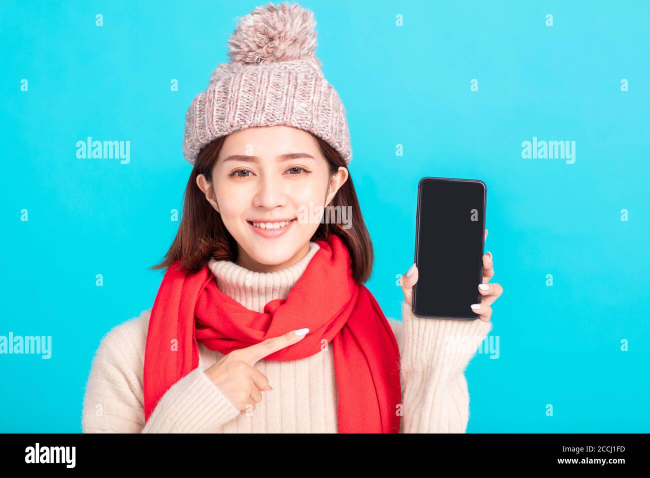Smiling young woman in winter dress and showing  smart phone Stock Photo
