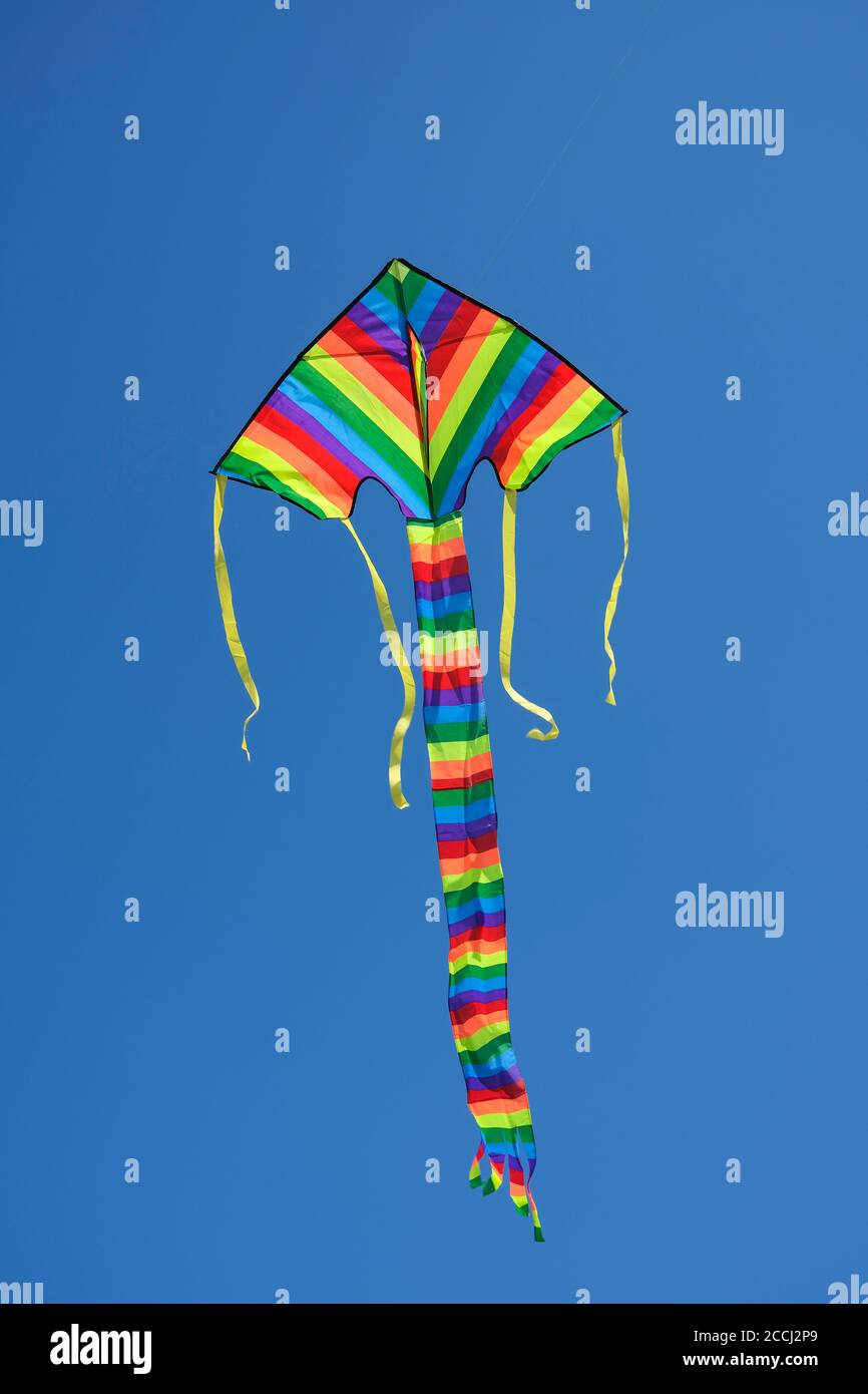Flying multicoloured kite against clear blue sky Stock Photo