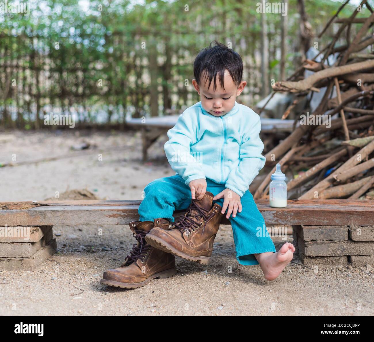 Asian baby boy try to wearing father boots while drinking milk from bottle  Stock Photo - Alamy