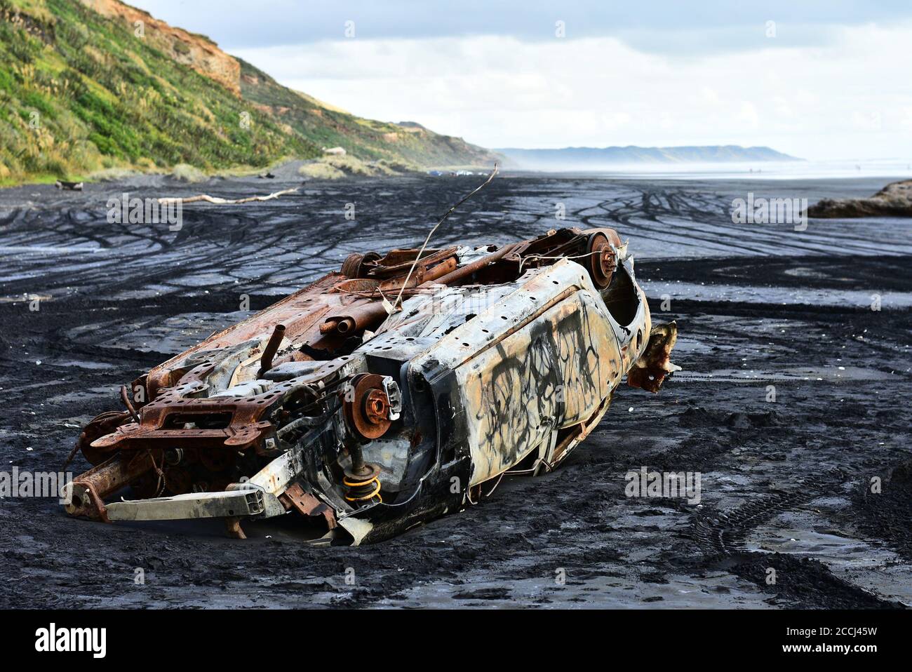 A car caught by high tide and left abandoned on black sand of Karioitahi beach, New Zealand. Car wreck buried in black sand, semi-submerged in sand. Stock Photo