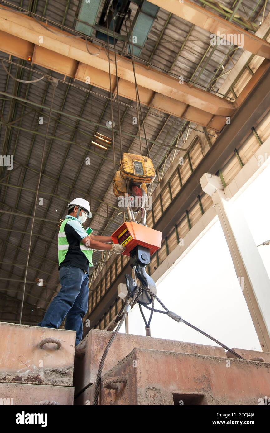 An Asian male engineer wearing protective equipment controlling electric cable hoist, heavy hoist iron hook lifting of structure platform. Stock Photo