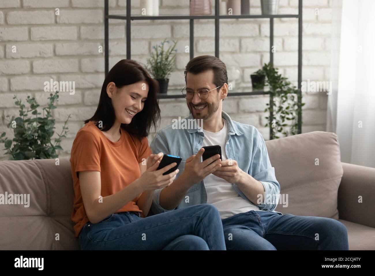 Happy millennial couple relax on sofa using cellphones Stock Photo