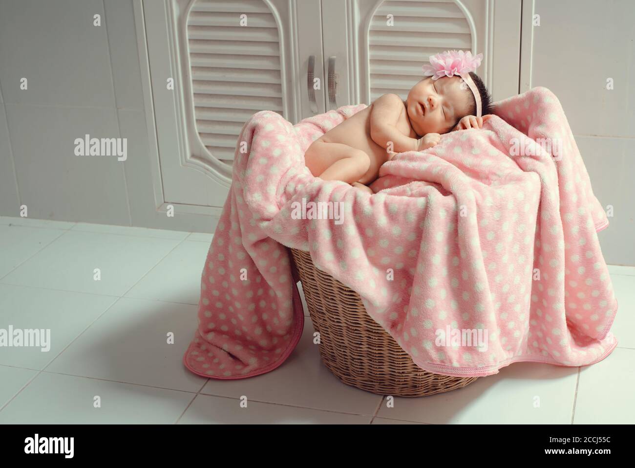 Beautiful newborn baby sleeping on a pink blanket in a wicker basket. Stock Photo