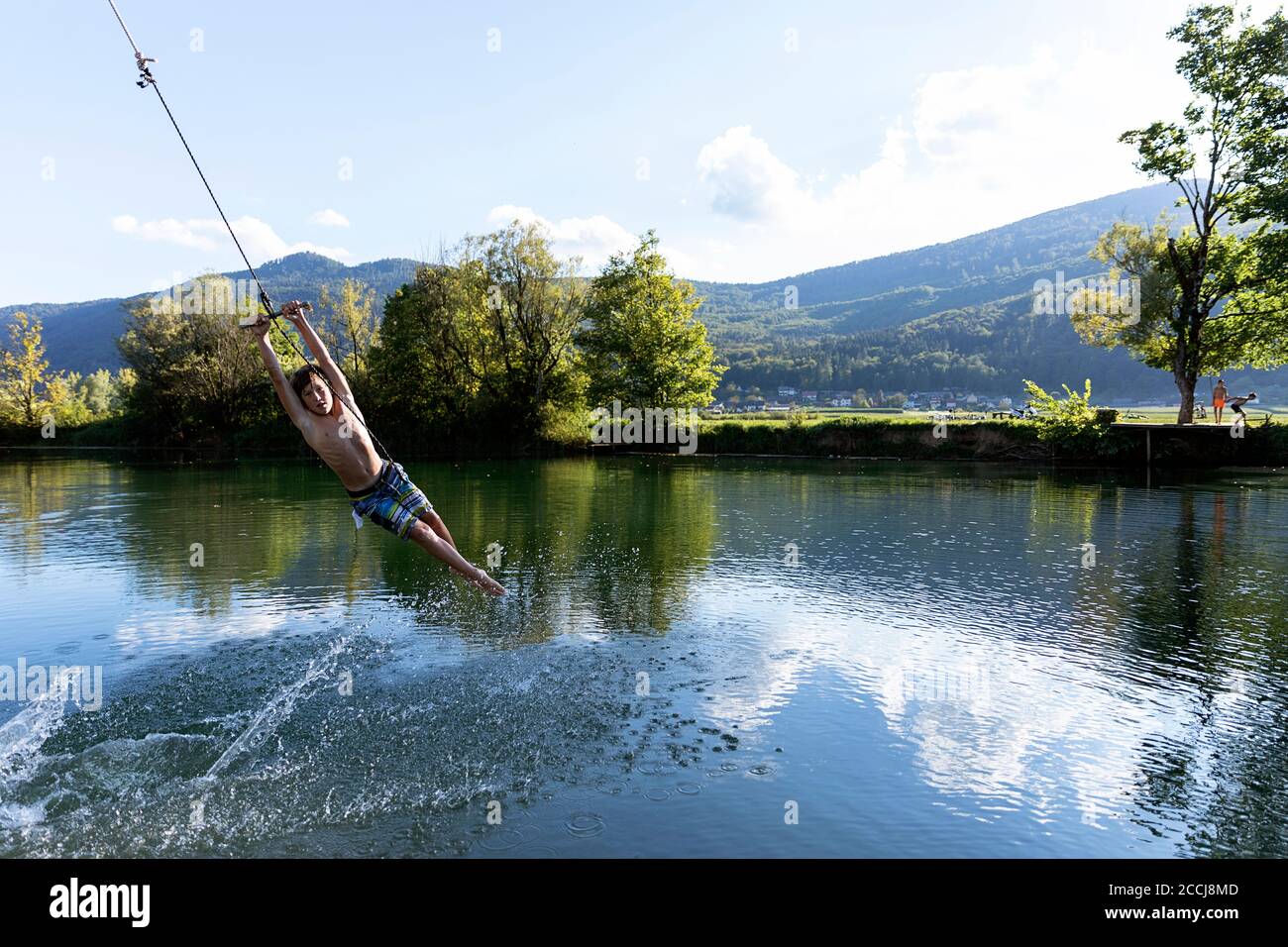 Summer by the river, boy swings on a rope swing over the Krka River