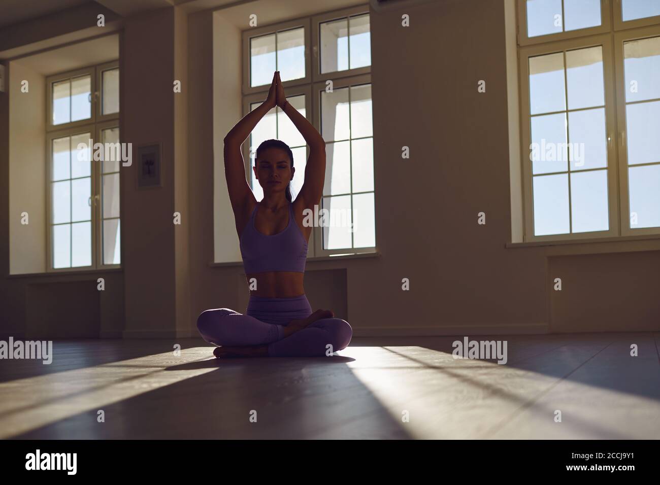 Girl doing yoga sitting in lotus position in a room in the morning at dawn. Stock Photo
