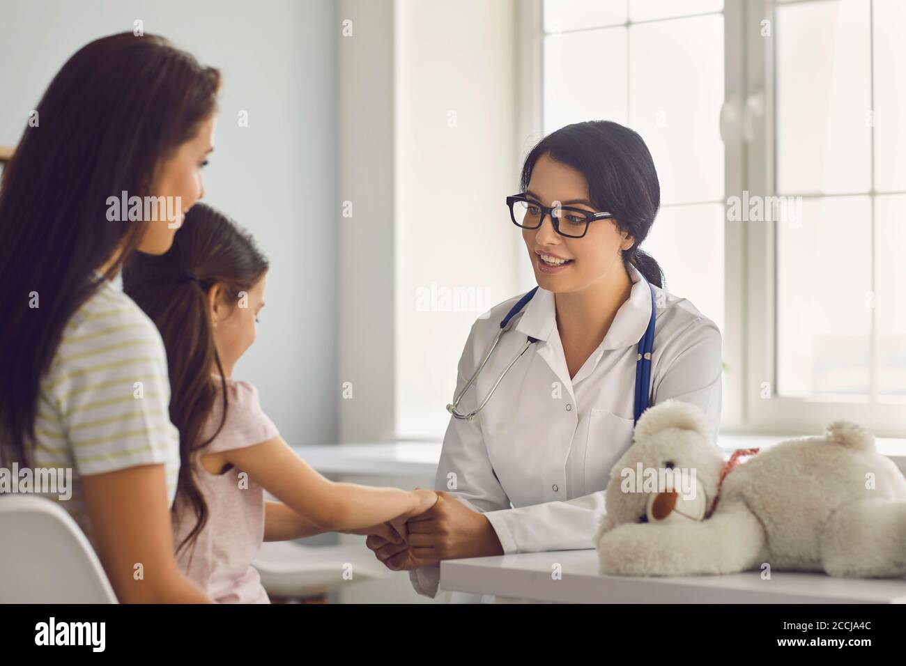 Family patients are consulted by a general practitioner in a medical clinic. Woman doctor smiling at the girl and her mom sitting at the table in the Stock Photo