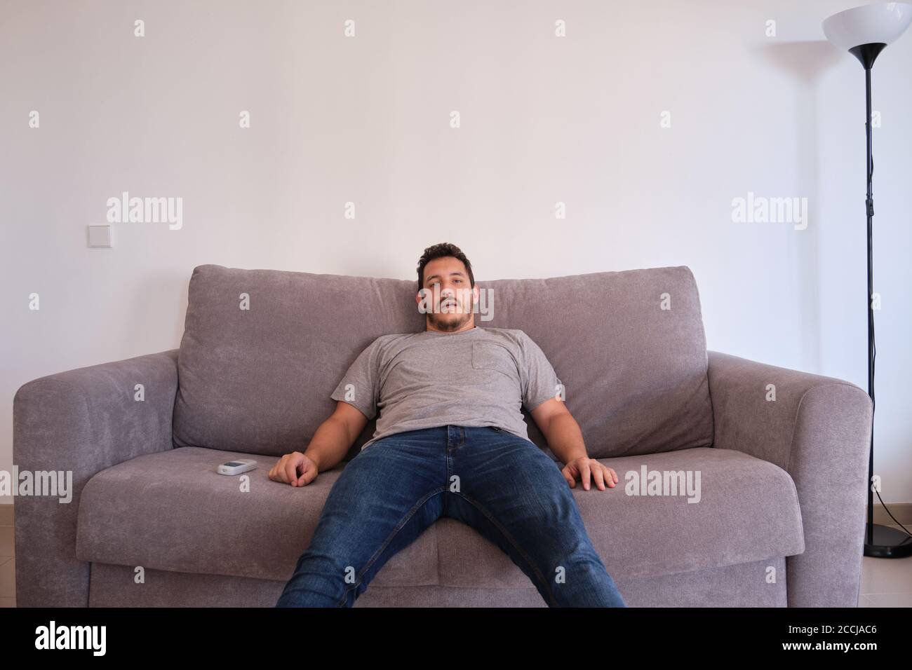 Portrait of a bored and tired young man sitting on a sofa watching television absorbed with his mouth opened. Stock Photo