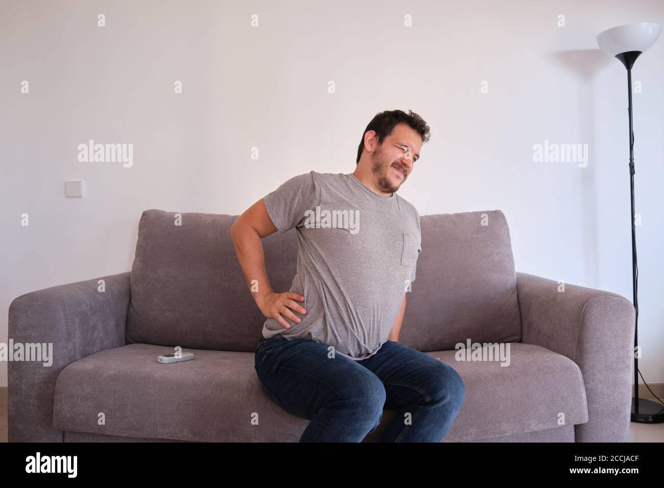 Young man sitting on a sofa suffering from low back pain. Backache concept. Stock Photo