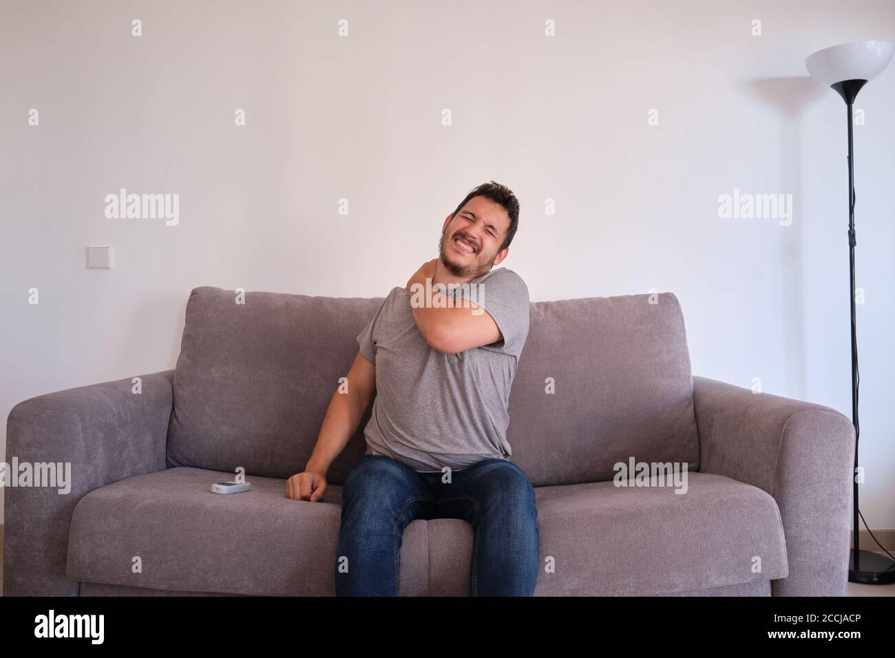 Young man sitting on a sofa suffering from neck pain. Neck and shoulder paint. Stock Photo