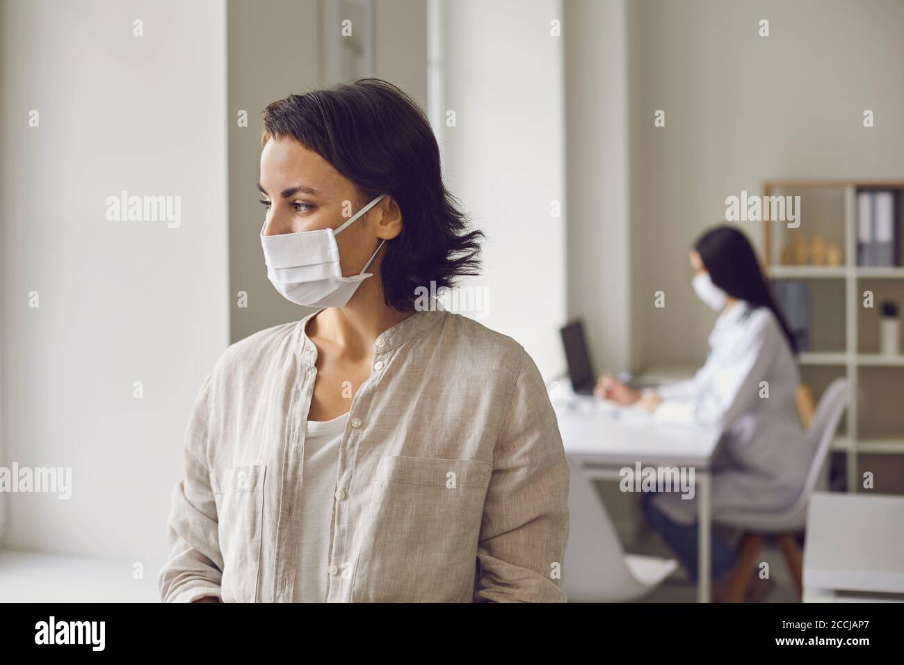 Woman patient in medical mask looking at window in medical clinic