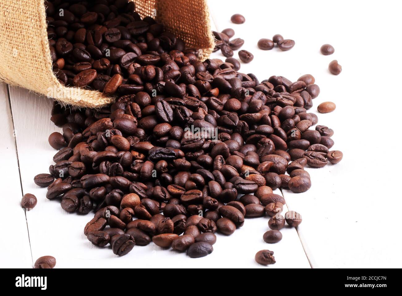 a collection of roasted coffee beans in a crochet bag on a white wooden plinth. Roasted coffee beans scattered of the burlap bag isolated on white Stock Photo