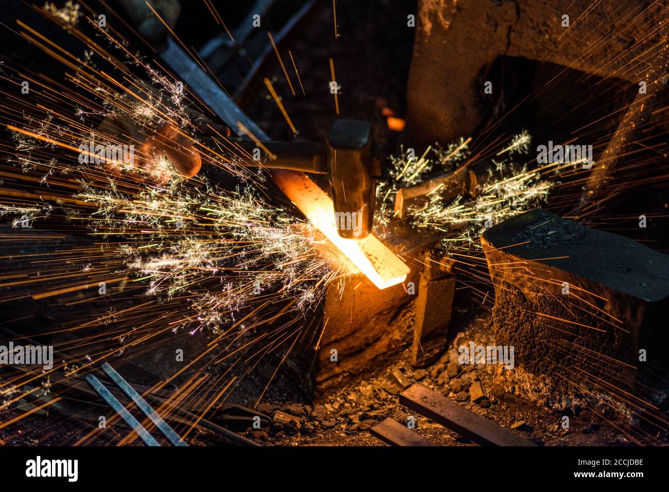 Blacksmith manually forging the molten metal on the anvil with spark ...